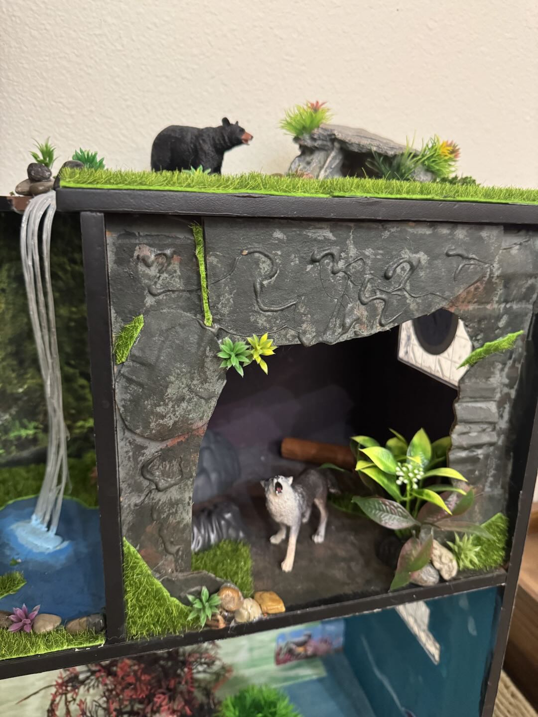A rocky cave habitat with a howling wolf, hanging greenery, and a side waterfall