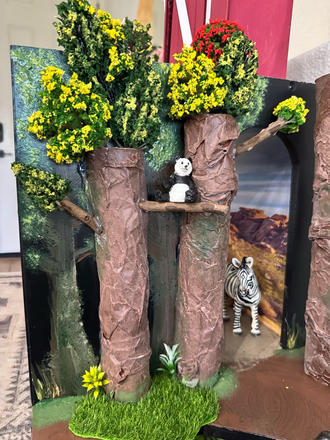 Tall sculpted tree trunks topped with bright yellow and red foliage, a panda perched on a branch, and a zebra below